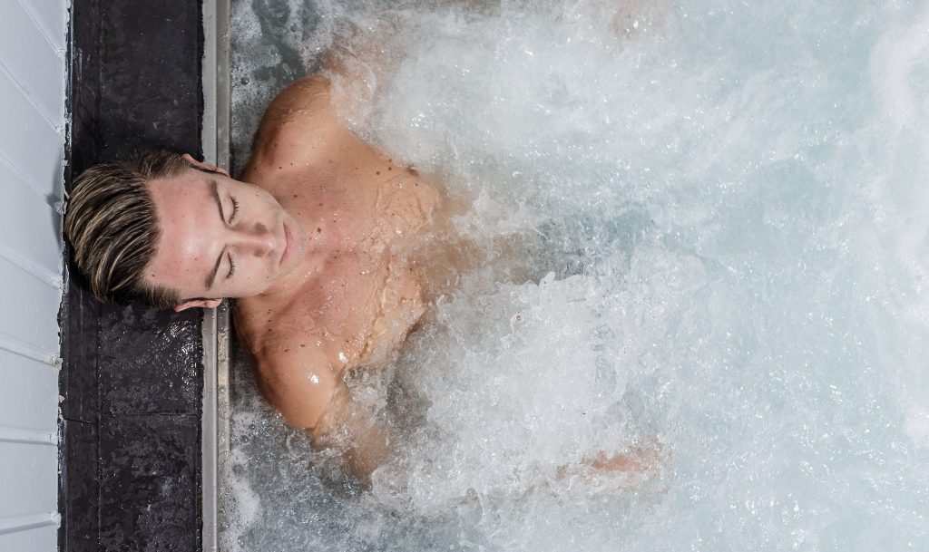From above young man relaxing in bubbling jacuzzi during spa session in wellness center